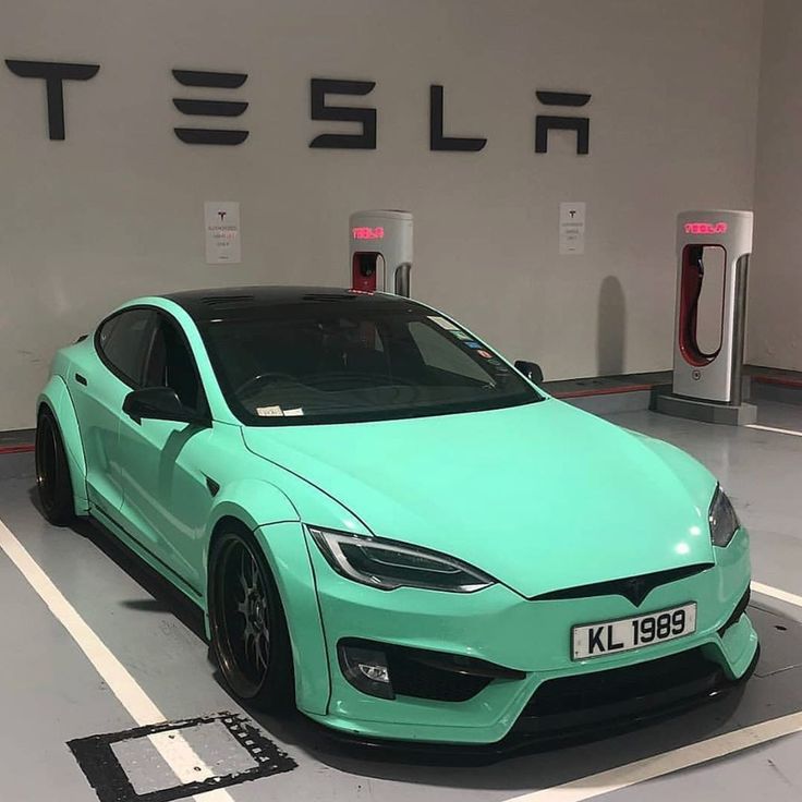 a green tesla car is parked in a parking lot