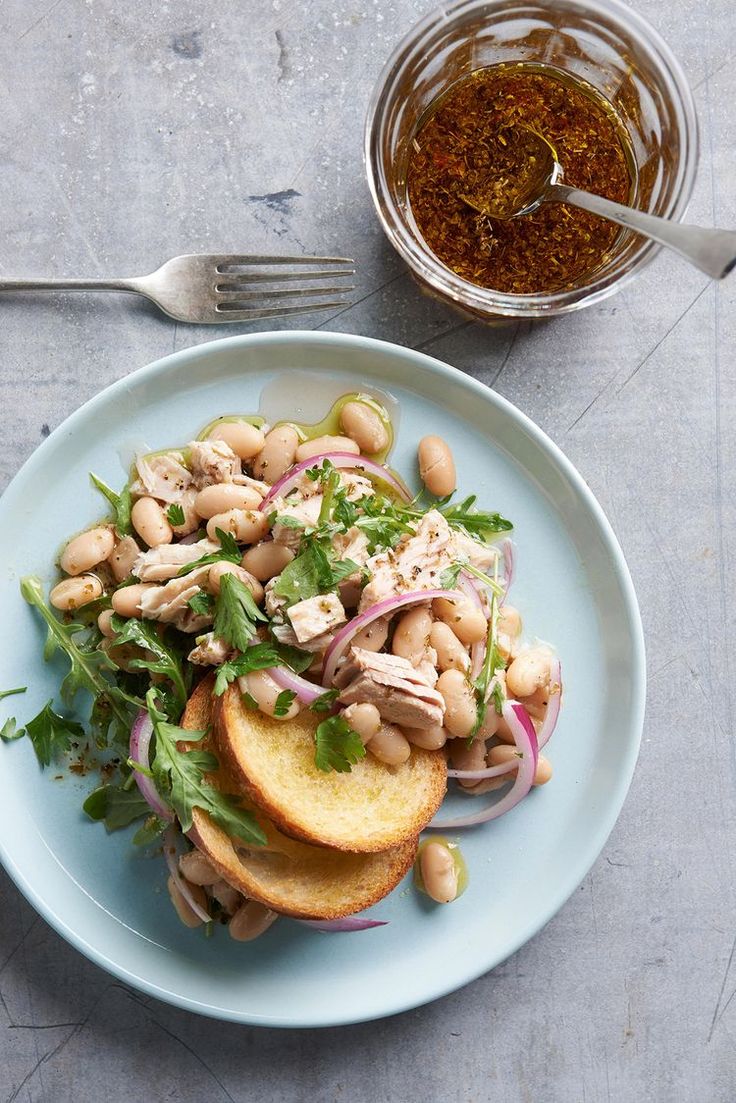 a blue plate topped with beans and greens next to a bowl of seasoning on a table