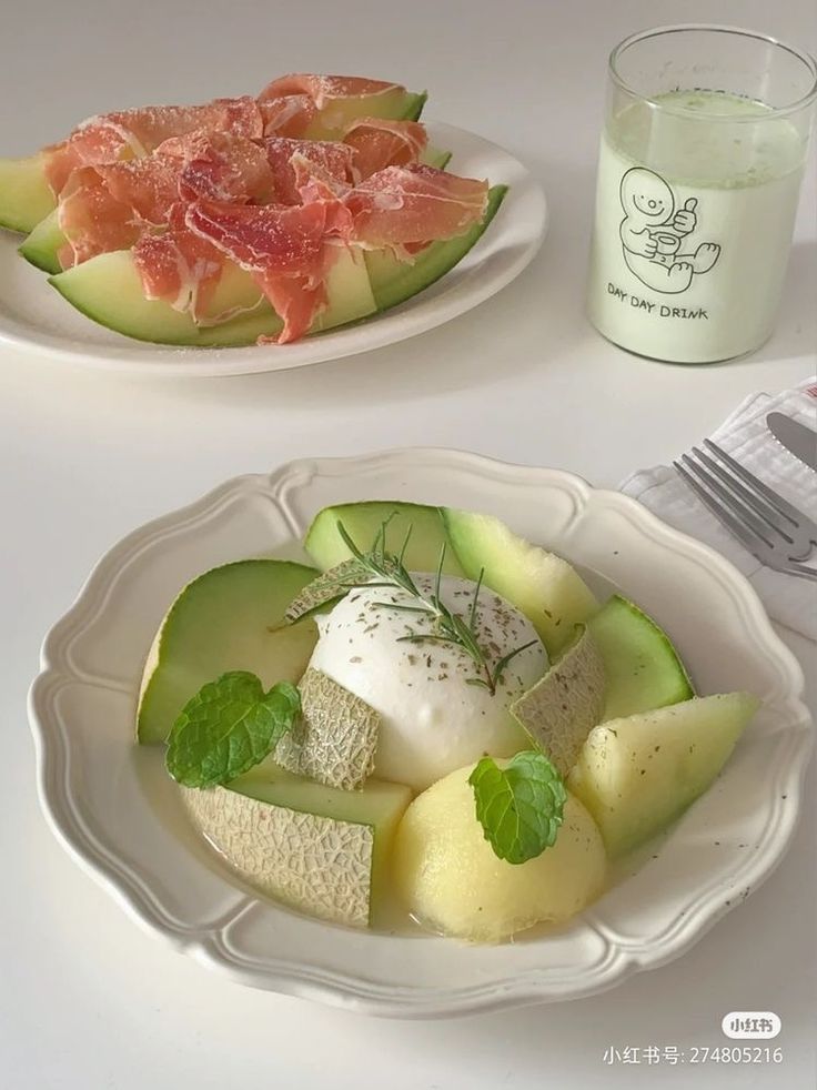 two white plates with food on them next to a glass of water and a fork