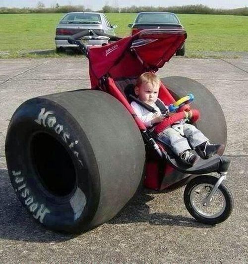 a baby in a stroller sitting on top of a large tire with two wheels