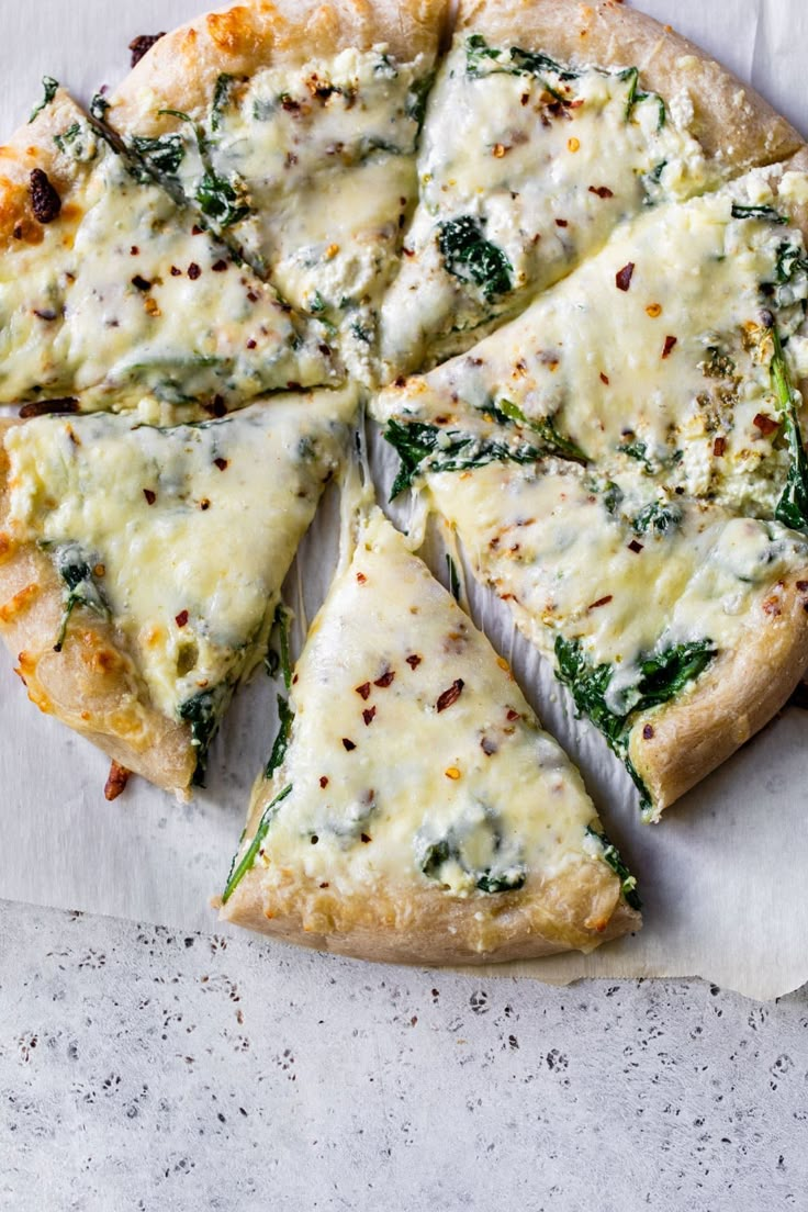 a pizza with cheese, spinach and other toppings cut into four slices on a piece of parchment paper