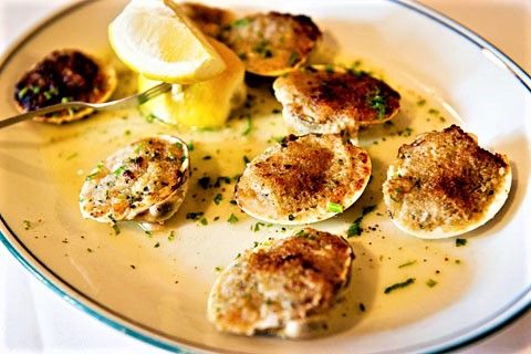 a white plate topped with scallops covered in sauce and lemon wedges next to a slice of lemon