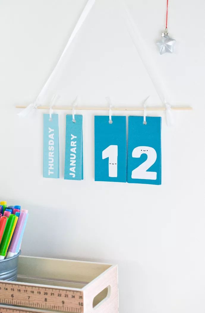 two calendars hanging on a wall next to a ruler and pencils in a container