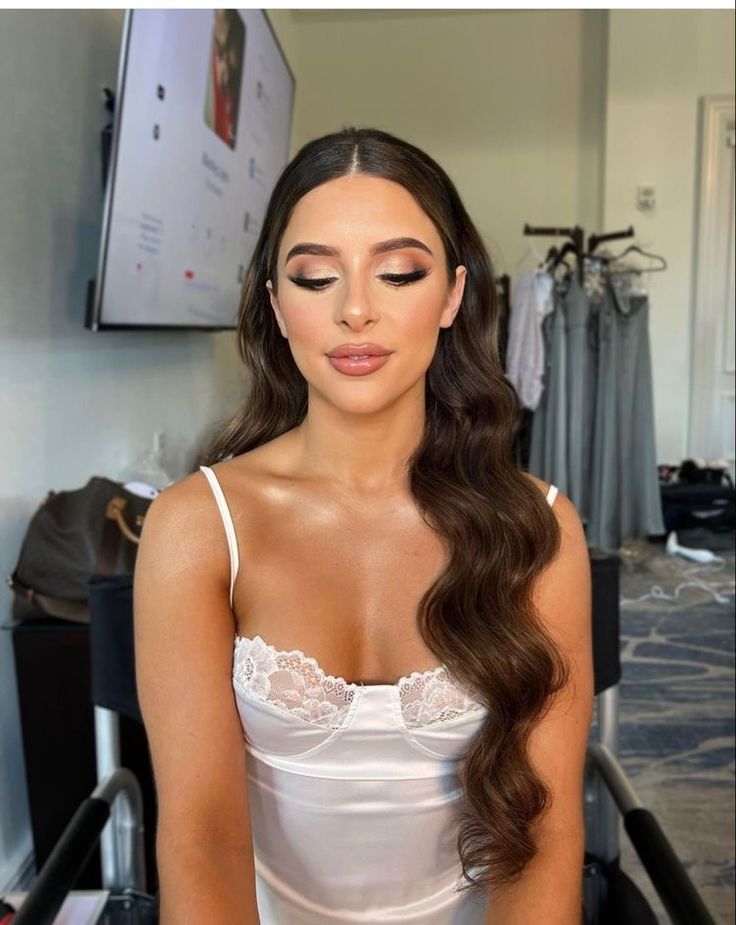 a woman with long brown hair wearing a white dress sitting in front of a mirror