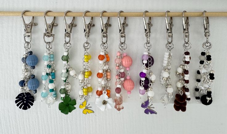 a row of key chains hanging from a wall next to a wooden stick with beads and charms on it