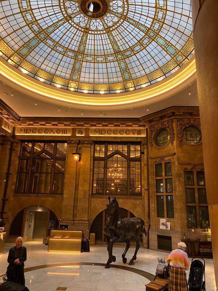 people are sitting in the lobby of a building with a large glass ceiling and a statue of a horse