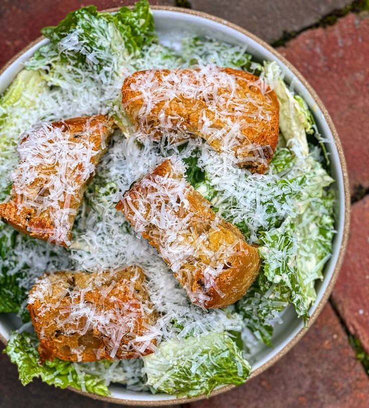 a bowl filled with lettuce and meat covered in parmesan cheese on top