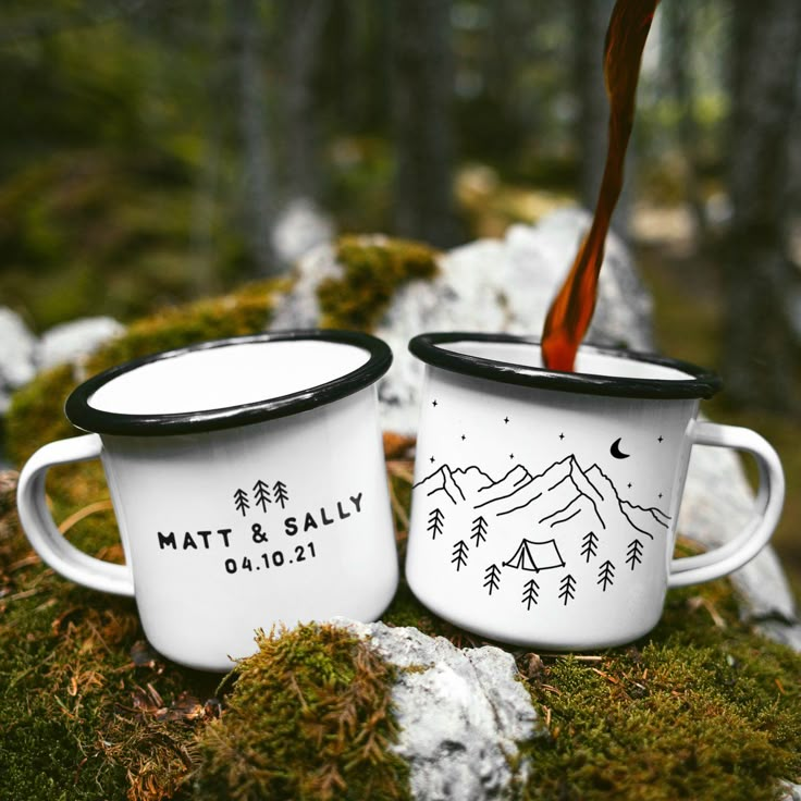 two coffee mugs sitting on top of a moss covered ground