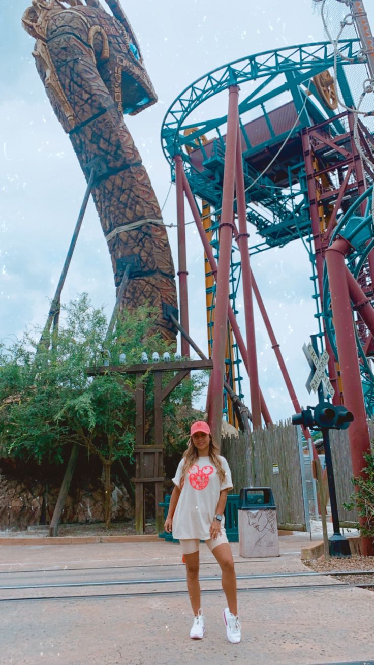 a woman standing in front of a roller coaster