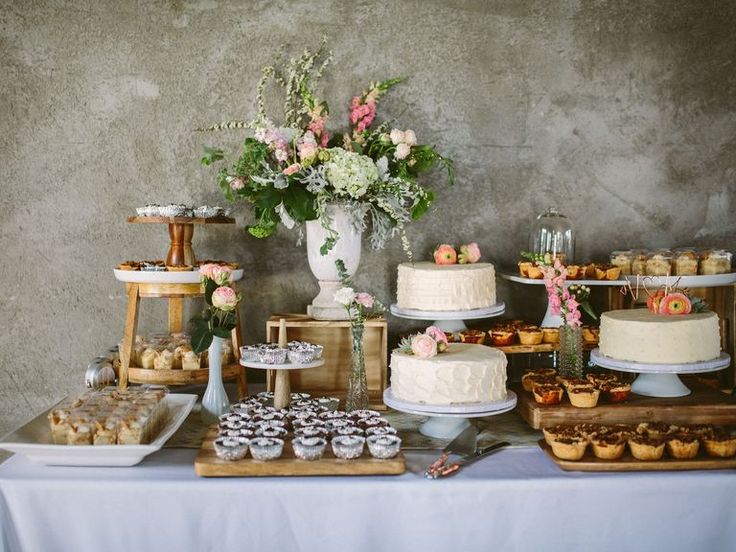 a table topped with cakes and cupcakes next to a vase filled with flowers