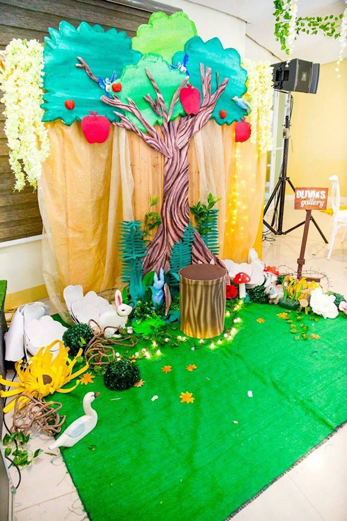 a stage set up for a children's birthday party with trees, flowers and decorations