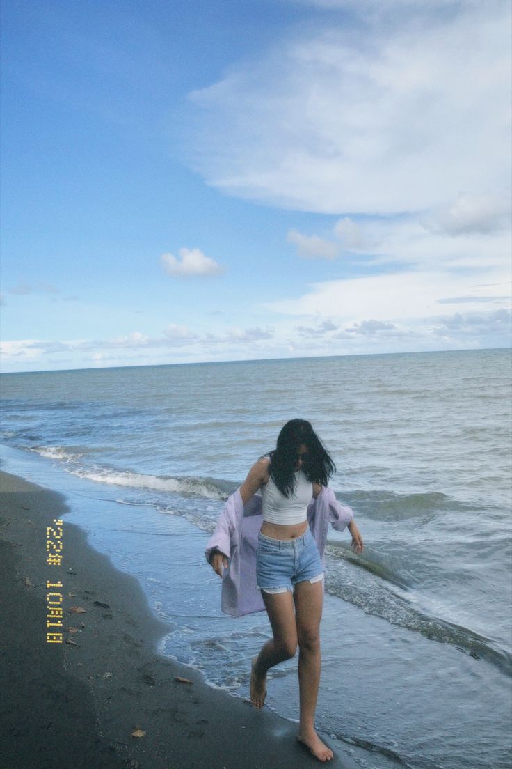 a woman is walking along the beach in shorts