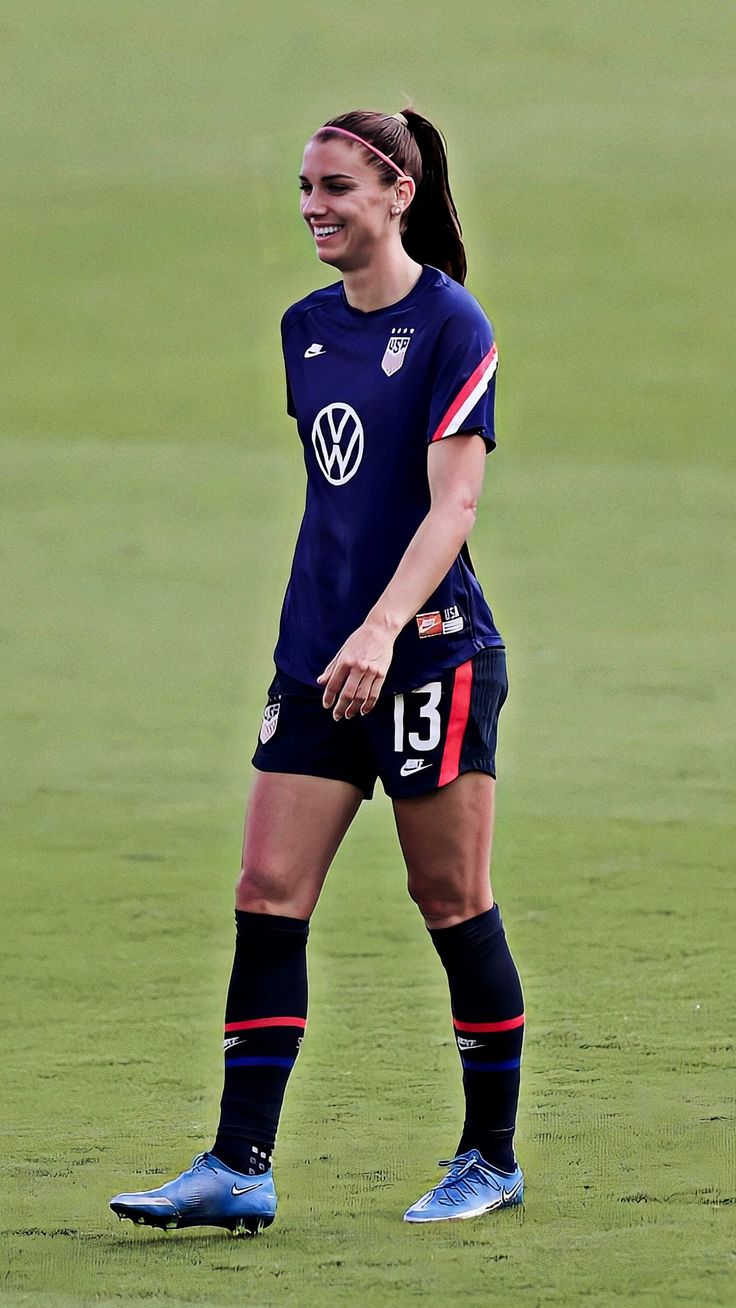 a female soccer player standing on the field with her foot in the air and smiling