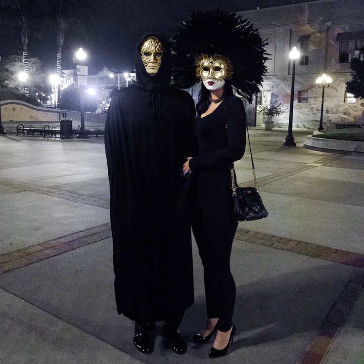 two women dressed in costumes standing next to each other on a sidewalk at night with street lights behind them