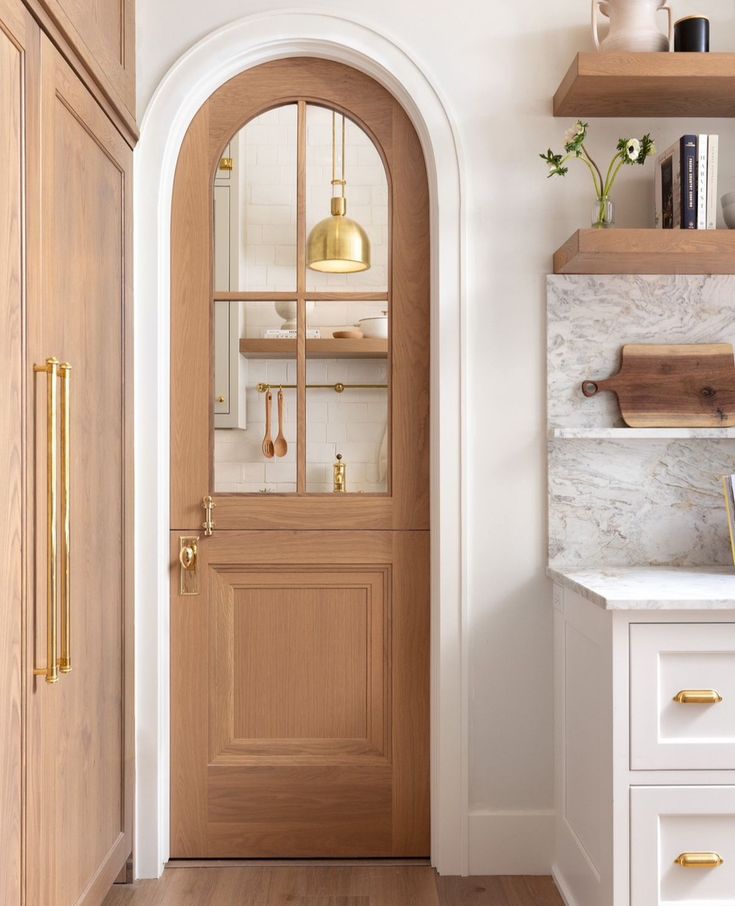 a wooden door in a kitchen next to a white counter top and cabinets with gold pulls