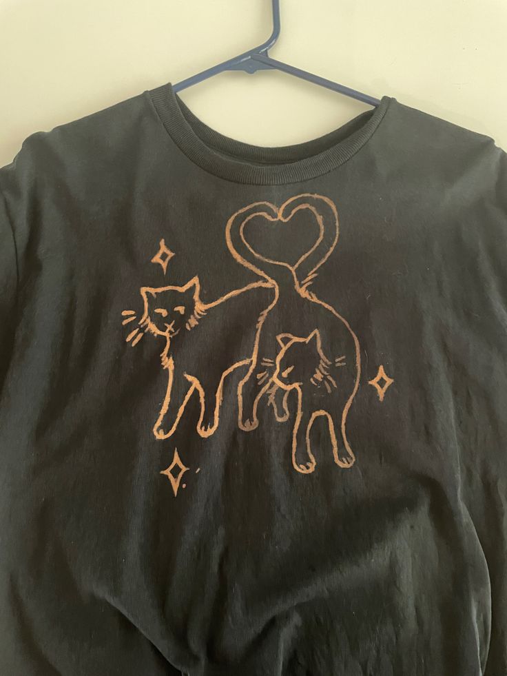 a t - shirt with an image of two cats on it hanging from a hanger