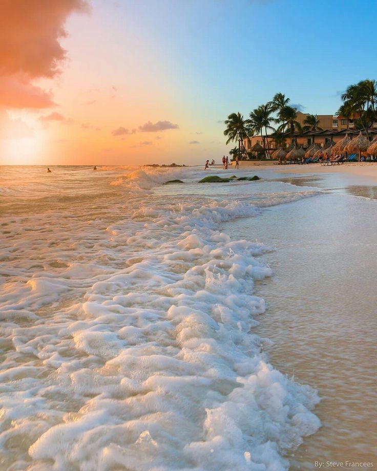 the sun is setting on an ocean beach with waves crashing in front of it and palm trees