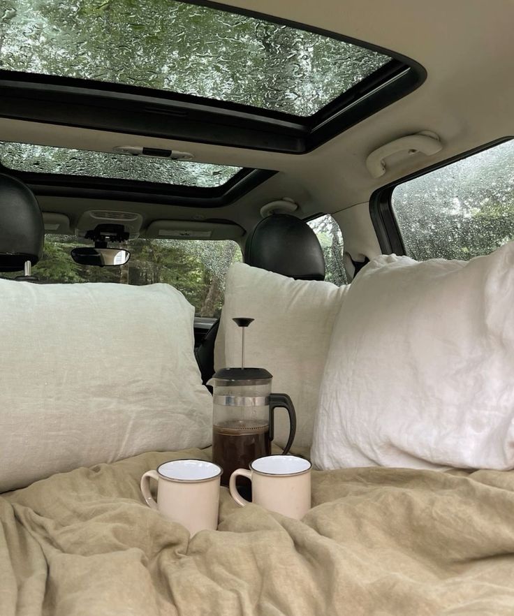 two coffee mugs are sitting on the bed in a vehicle with pillows and blankets