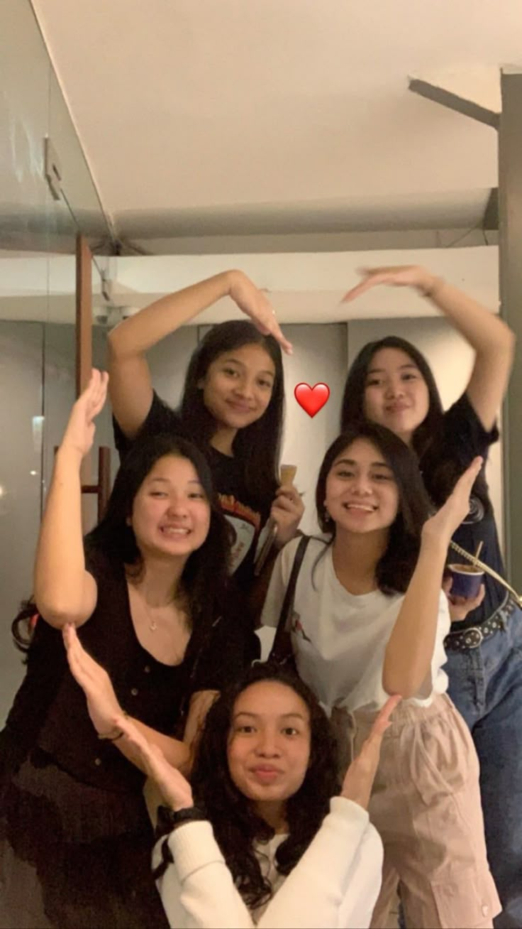 four women are posing for a photo in front of a mirror and holding their hands up