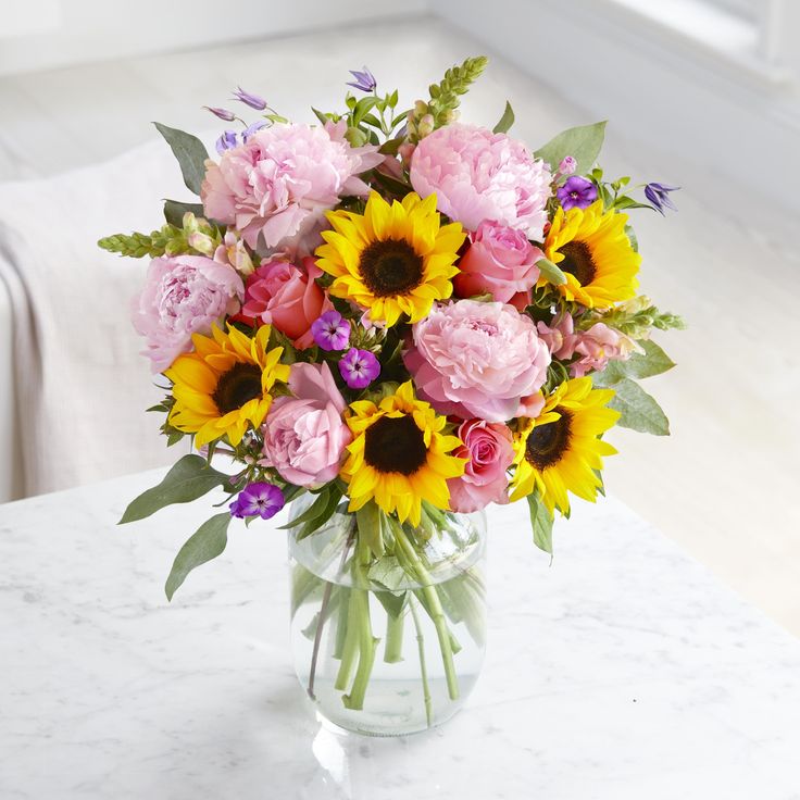 a woman holding a bouquet of flowers in her hand with pink and yellow blooms on it