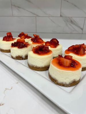 small cheesecakes with strawberries are arranged on a white platter in the kitchen