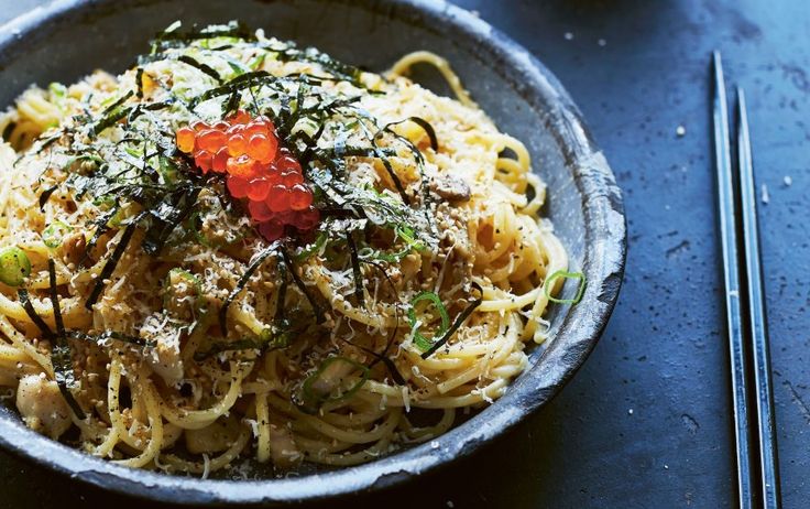 a bowl filled with pasta and sauce on top of a blue table next to chopsticks