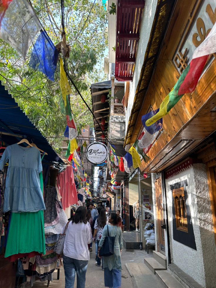 several people walking down a narrow street lined with shops and colorful flags hanging from the buildings