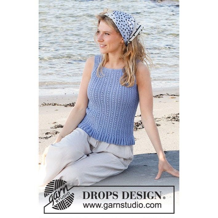 a woman is sitting on the beach wearing a blue sweater and white hat with polka dots