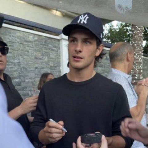 a man in a black shirt and hat holding a cell phone while standing next to other people