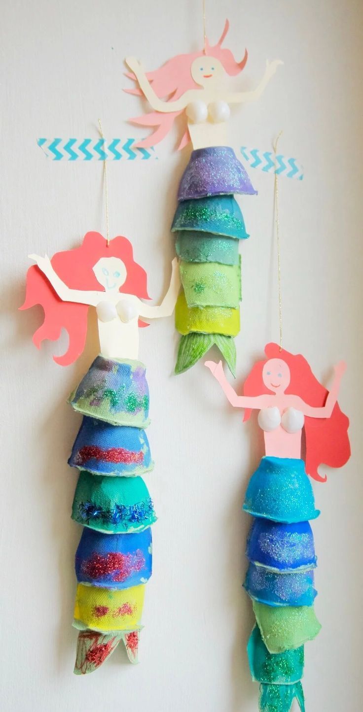 two little mermaids hanging from the side of a wall with paper decorations on them