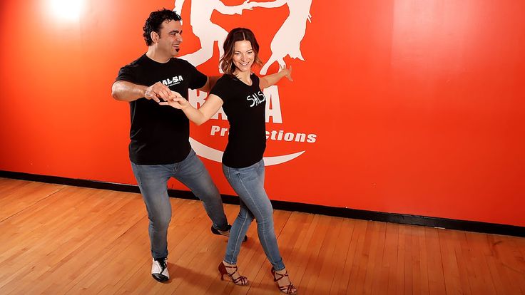 two people dancing on a wooden floor in front of a wall with an orange background