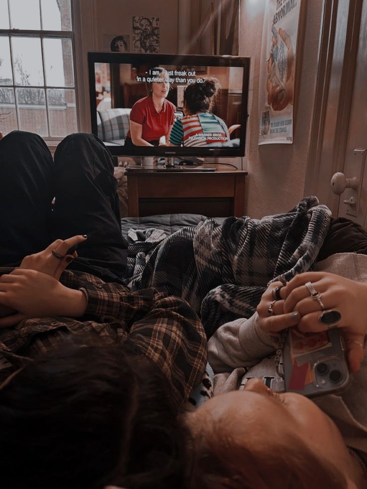 two people laying on a couch watching tv with their hands in each other's pockets