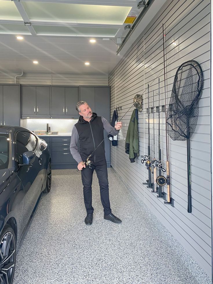 a man standing next to a car in a garage with lots of fishing gear hanging on the wall