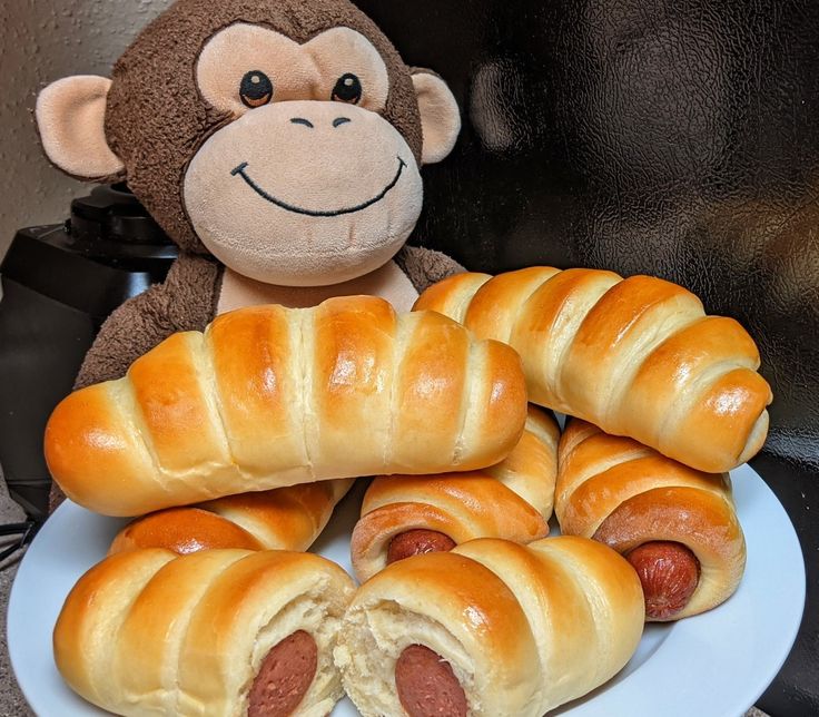 a plate with hot dogs wrapped in bread and a stuffed monkey