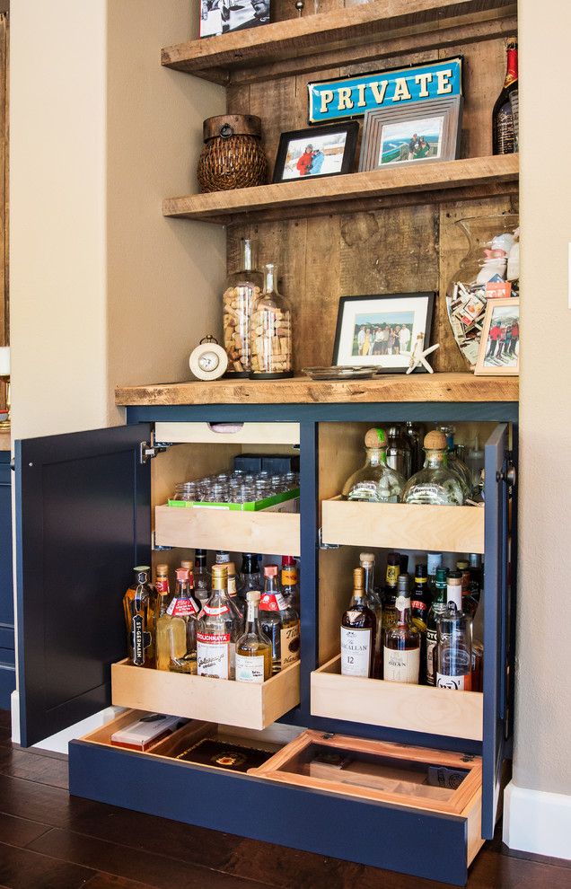 an open cabinet with liquor bottles and pictures on the top shelf, in front of a wall