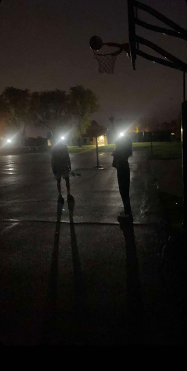 two people are standing in the dark with their lights on and one person is holding a basketball