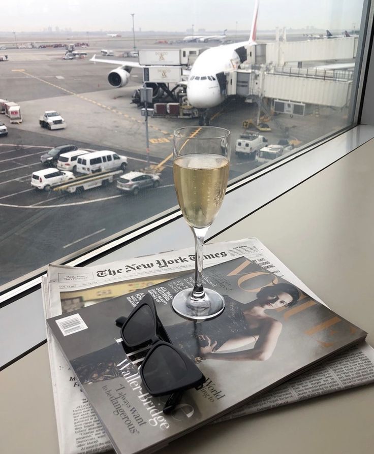 a glass of wine sitting on top of a news paper next to an airport window