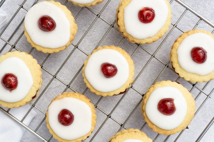 small cookies with white icing and cherries on a cooling rack, ready to be eaten