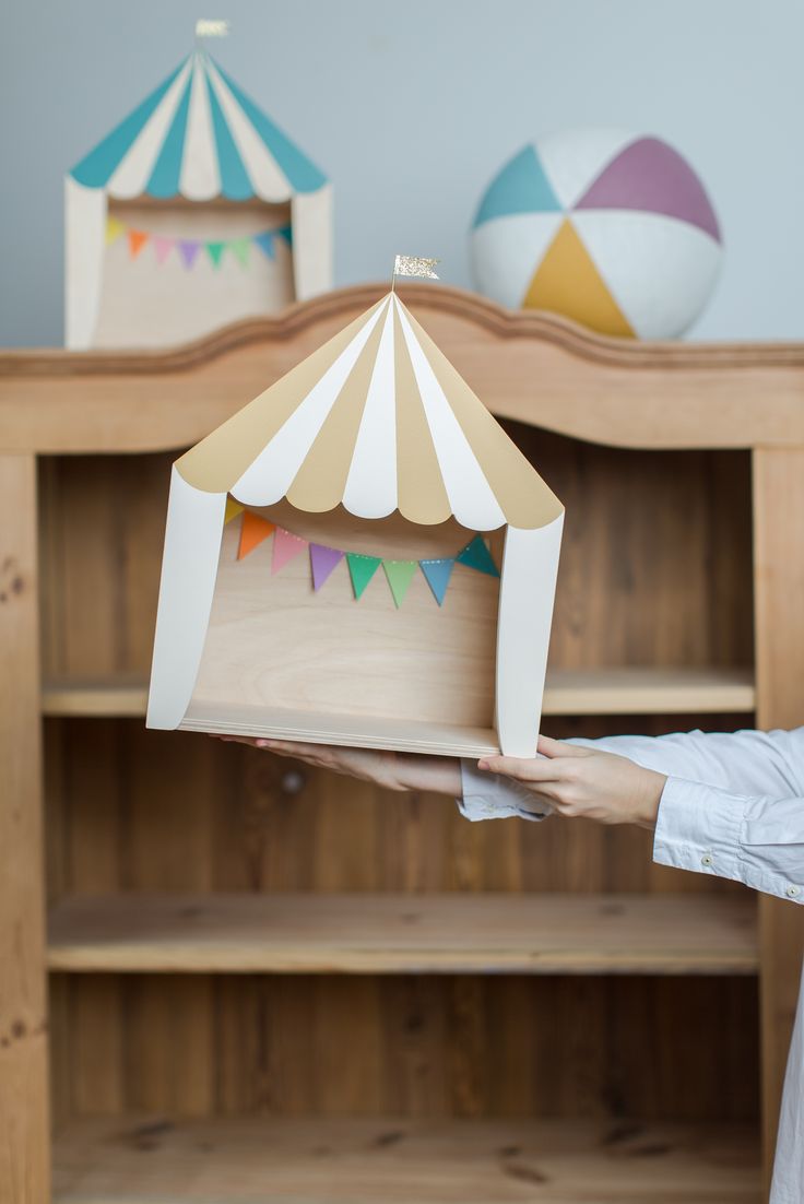 a person holding up a wooden box with a tent on top of it in front of a bookcase