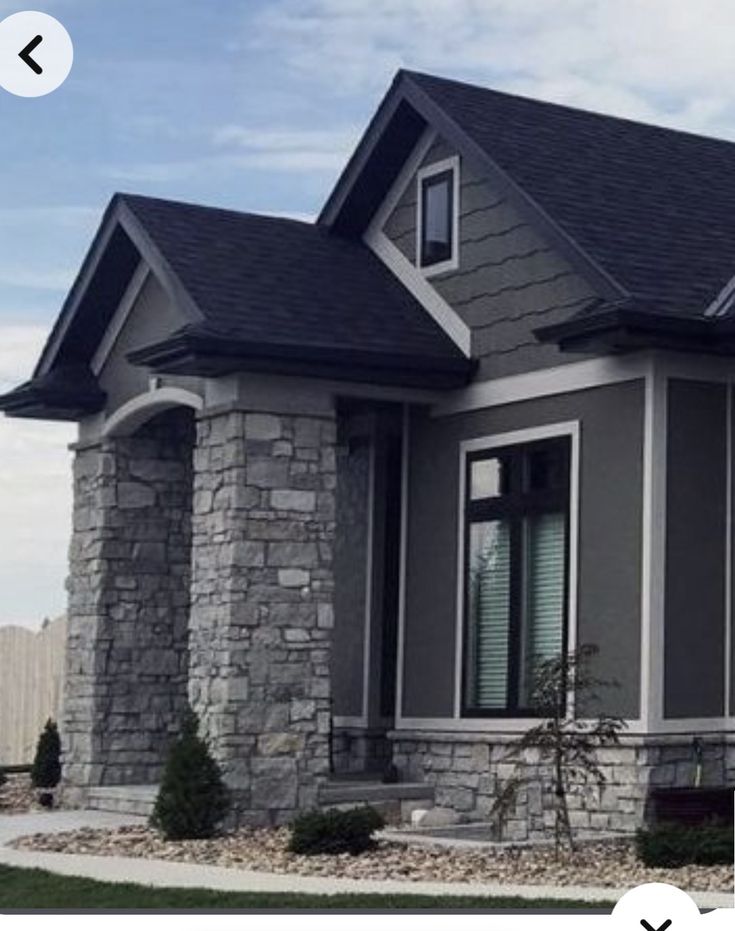 a gray house with black shingles and stone accents on the front porch, along with green grass