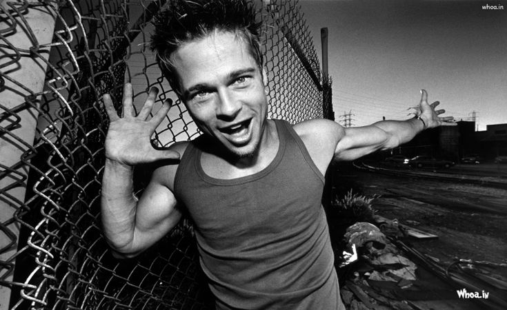 a man making the peace sign with his hands while standing in front of a chain link fence