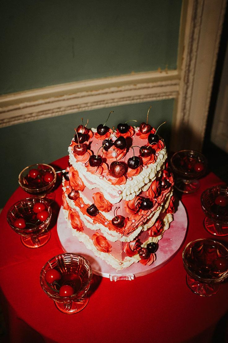 a heart shaped cake with cherries on top sits on a table surrounded by glasses