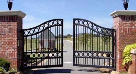 an iron gate in front of a brick building with two lamps on top of it