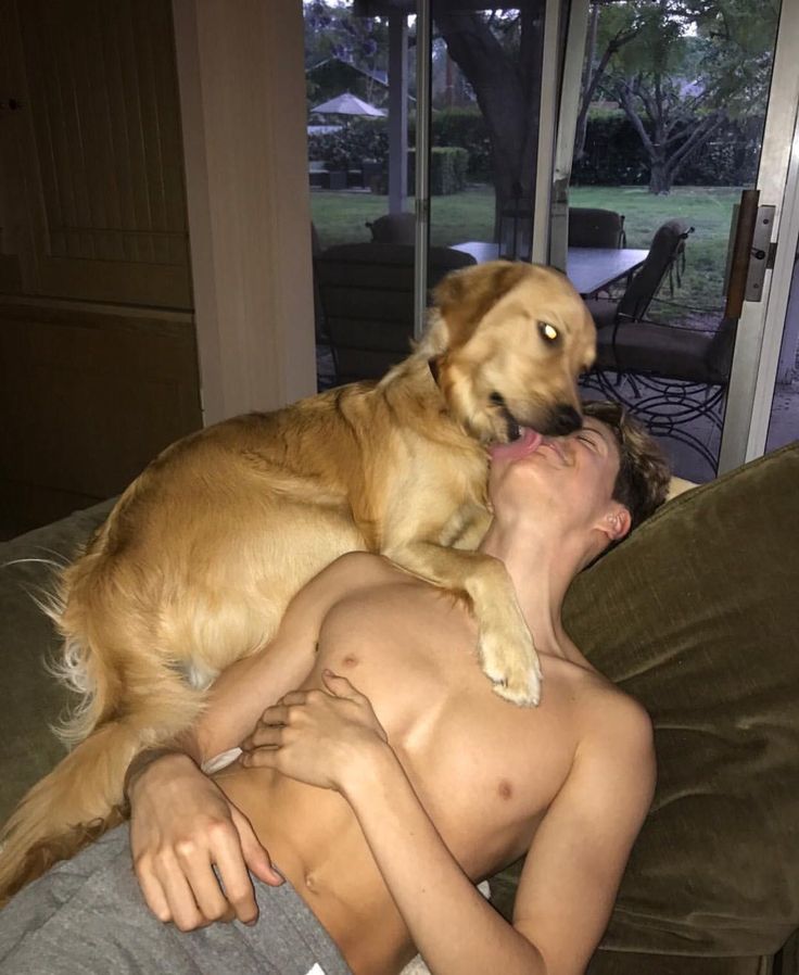 a young boy laying on top of a couch next to a large brown dog with it's mouth open