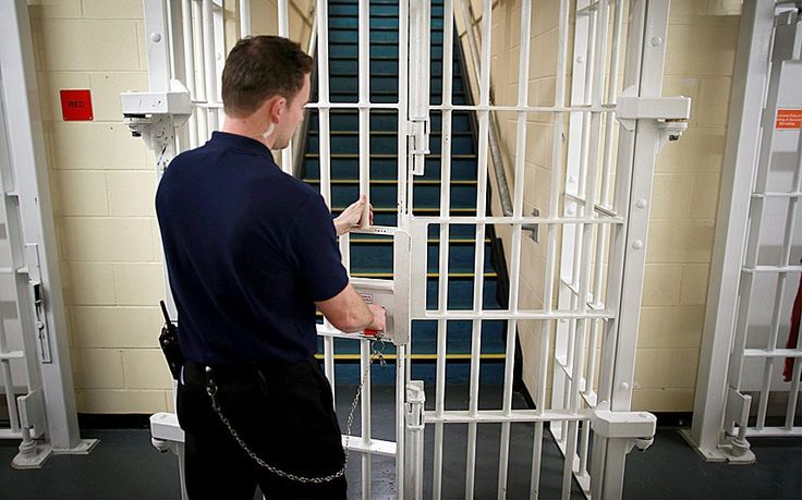 a man standing in front of a jail cell with his hand on the door handle