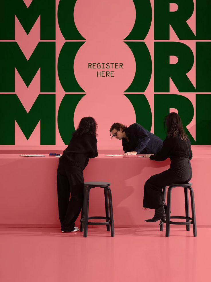 two people sitting on stools in front of a pink wall with the words moremore