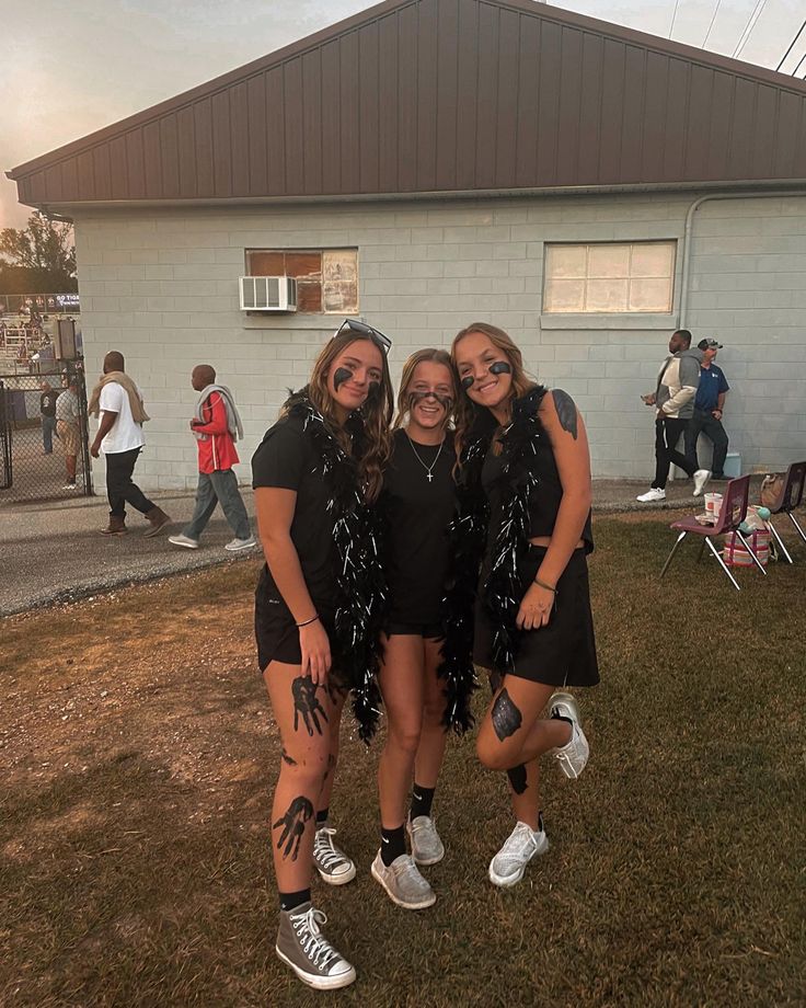 three girls are posing for the camera in front of a building with people standing around