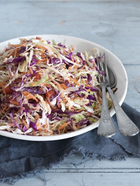 a white bowl filled with coleslaw slaw next to two silver spoons