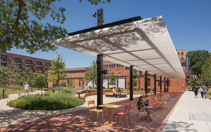 people are sitting at tables under an awning on the side of a brick building