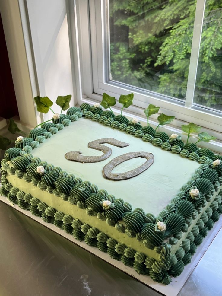 a large green cake sitting on top of a table next to a window with leaves